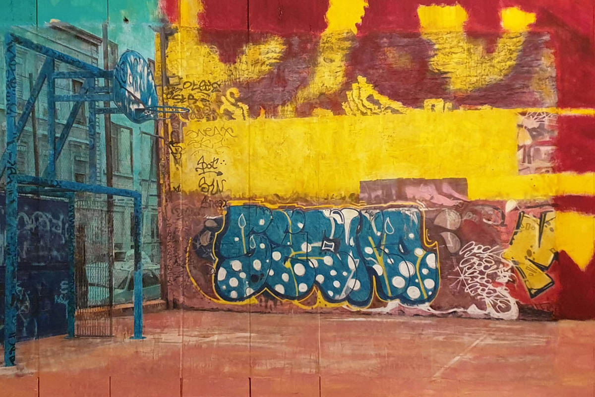 Street flashy. Un terrain de basket tagger à Lyon. Des couleurs vives, gaies et joyeuses apportent une modernité à cette ambiance street-art. C’est une photo prise en noir et blanc, repeinte manuellement aux pastels, crayons de couleurs, peinture. Œuvre sur une palissade faite en bois de palette. Un tableau réalisé par Gaïa du Rivau, photographe, plasticienne, photographiste à Nyons